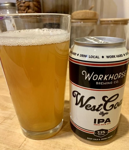 Hazy golden colored IPA in a pint glass and its can are on a maple wood table. The can has a retro looking with navy and cream colored design.