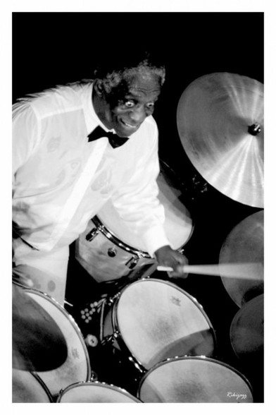 Low angle b&w photo of Art Blakey playing on his drumset.
It's a live action photo, full of energy, full of vibrations