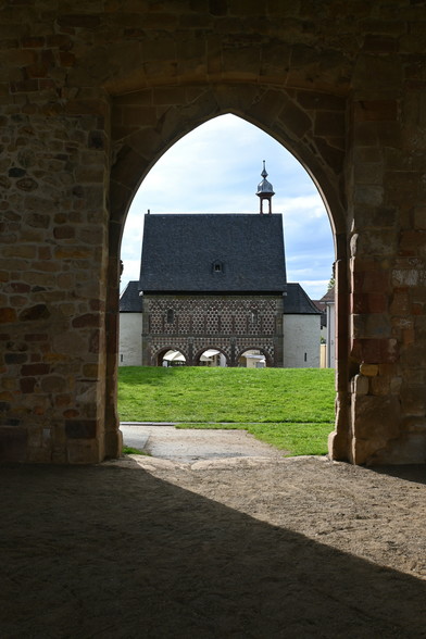 Looking through a pointed arched doorway towards a building with three rounded arches on the ground floor 
