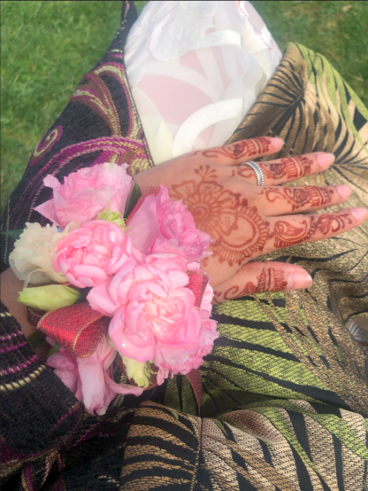 Hennaed hand with pink and white corsage against a multicoloured fabric.