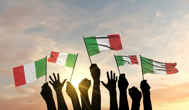 Hands holding up individual Italian flags, backlit by the sun