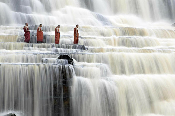 Monks in their orange robe praying on the terraced waterfall