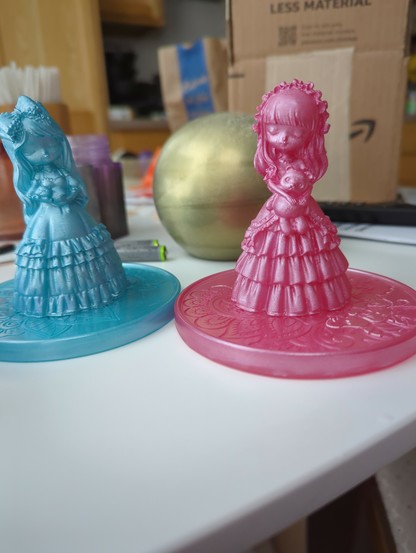 Two stylized epoxy figurines of old fashioned girls. One is glossy blue, the other glossy pink.