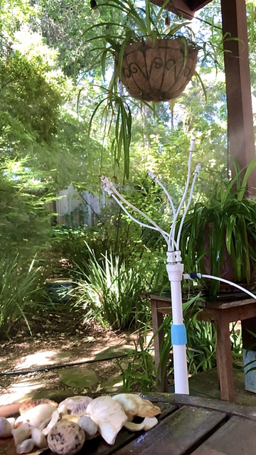 Photo of back yard and a water mister that is a 3 foot tall white plastic tube/stand with 5 flexible arms with nozzles that mist water. 