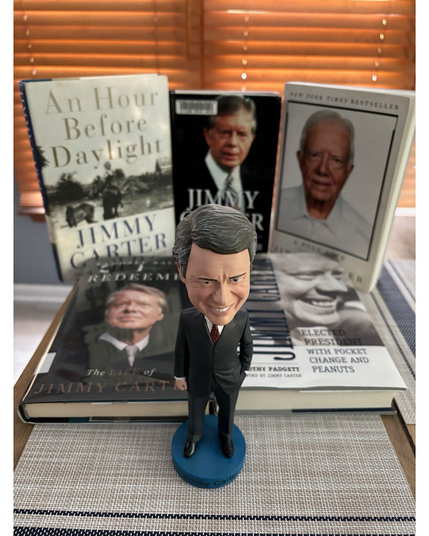 A Jimmy Carter bobblehead in front of five books about Carter on top of a table 