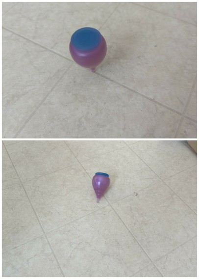 A top in action on a floor. It is purple with a blue cap. Inverted pear shape.