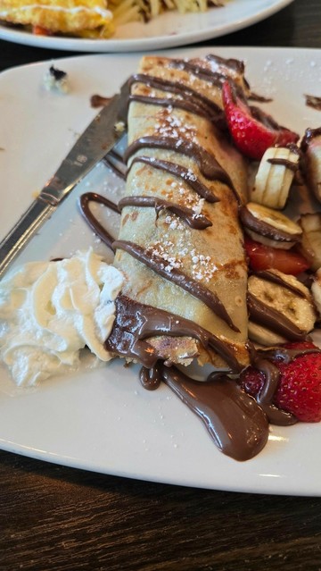 Nutella crepes with whipped cream, strawberries and bananas, all on a plate