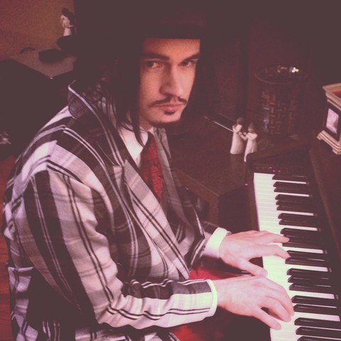 Mans dressed in black, red and white, seated at a piano