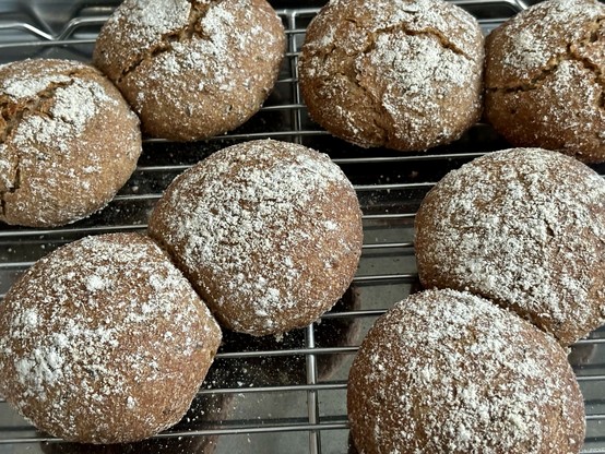 Freshly baked bread rolls with a dusting of flour on a cooling rack.
