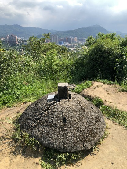 A stone marker at the top of Little Nangang Hill, with Taipei visible behind bushes.