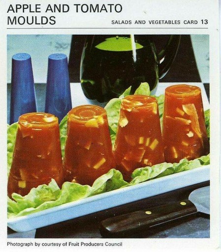 Vintage recipe card for apple and tomato moulds. A photo of four towers of tomato jelly with chunks of apple inside, sitting on a bed of lettuce. They’re the shape of disposable cups that they’re made in.