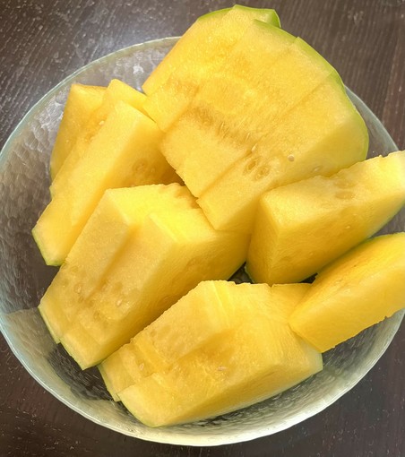 Cut yellow watermelons on a glass bowl on an espresso colored table.