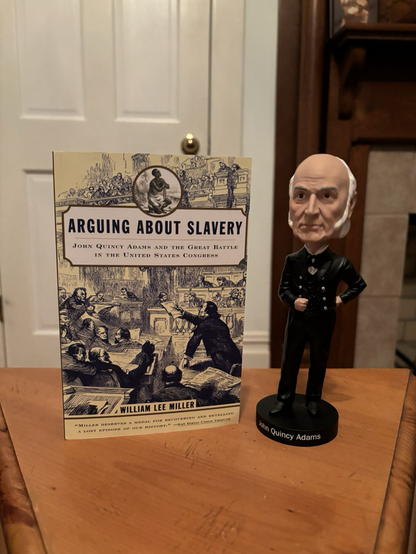 Book and a bobblehead of John Quincy Adams on a table 