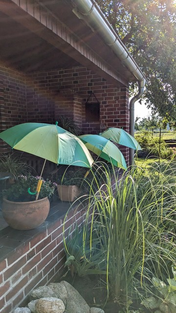 Flower pots on a brick porch, each one protected from the sun by a small colorful umbrella 