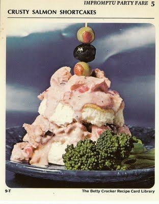 Vintage recipe card for Crusty Salmon Shortcakes. A photo of a pile of shortcake and salmon in a gooey pink sauce, served with olives on top and a side of broccoli.