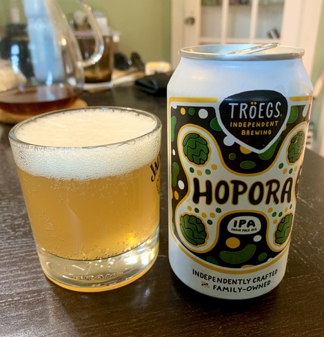 Troegs Hopora IPA in a whisky glass. Looks hazy and nice foamy beer head. The can has several cartoon hops. 