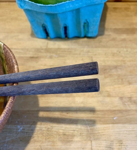 A bowl and chopsticks are on a wooden kitchen counter table.