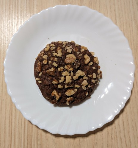 a large chocolate cookie covered in big walnut chunks sitting on a white plate. you can't see it on the picture, but it's about the size of the palm of my hand