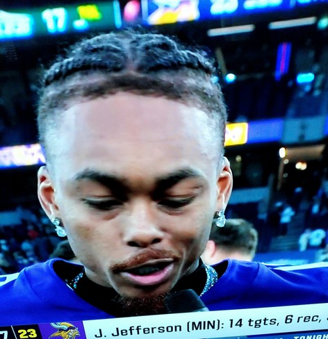 Justin Jefferson, Minnesota Vickings wide receiver being interviewed post game. He has accessorized his uniform by wearing two large dangling diamond or platinum earrings  and a diamond collar necklace.