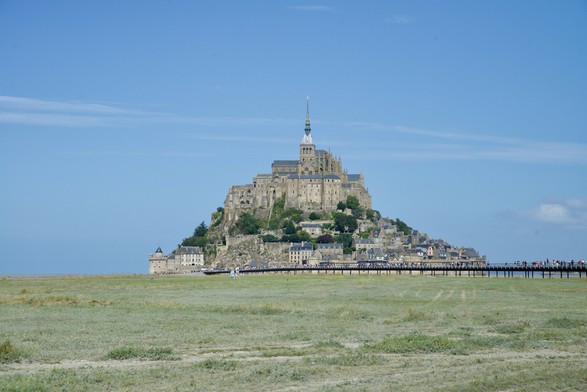 The Mont Saint-Michel seen from a distance, clear skies, tourists walking over a bridge.