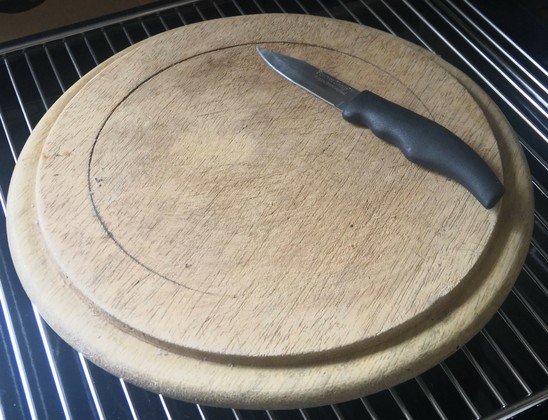 A circular wooden chopping block with many scratches in the wood grain. A small knife with black handle rests on it.