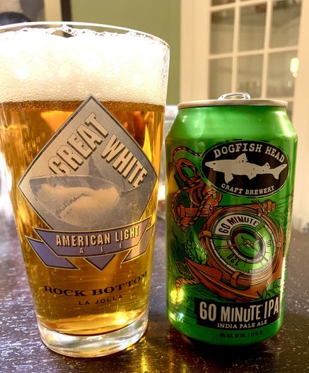 Dogfish head 60 minute IPA in a pint glass that has a great white shark. Its green can with an orange anchor is on the side.