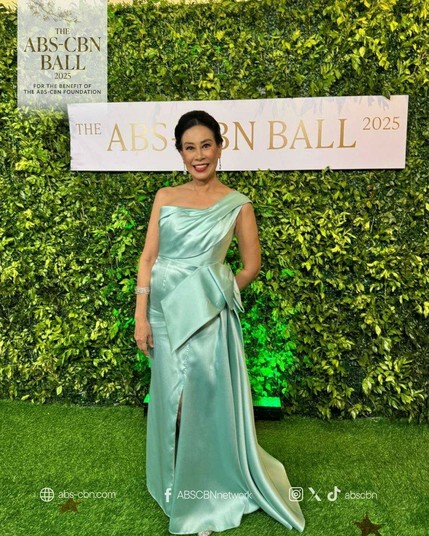 Susan Africa wearing a teal satin gown. The gown hangs on her right shoulder hugging her body with a huge bow of similar fabric on her right hip.