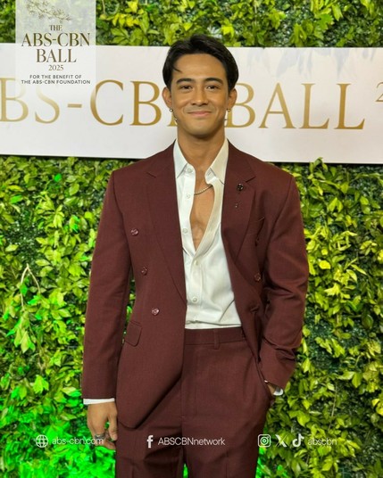 Argel Saycon wearing an ochre coat on top of a white button-up shirt with its first three buttons open to let the viewers a peek of his muscular chest accentuated by a simple silver chain.