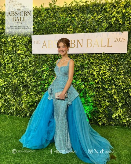 Fyang in a sparkly blue long gown with a thick pile of tulle in deeper blues as her train that makes it look like she is wearing a bouffant-style ball gown.