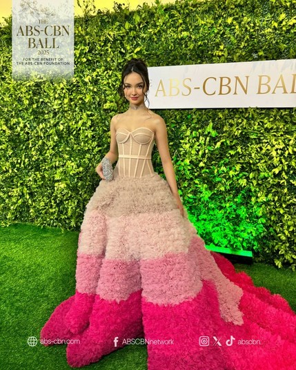 Kai Montinola in a ball gown. The bodice is a nude-colored corset with exposed bones, while the skirt is a bouffant-style fluff of nudes and pinks.