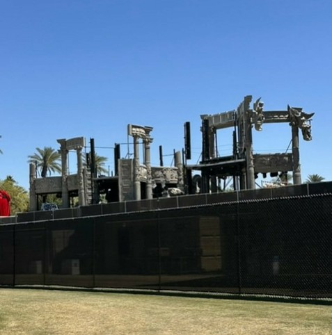 An under-construction structure made of a concrete-like material. The structure consists of corinthian pillars and angel gargoyles. The image is taken from outside a set of barricades.