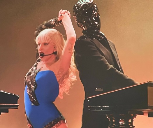 Lady Gaga wearing a blue leotard and Gessafelstein with his face fully covered in black metal, making him look like a moving statue.