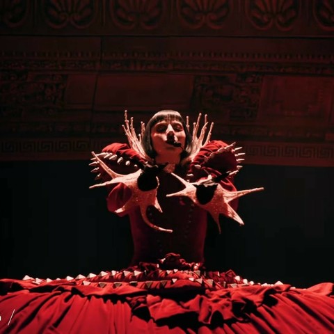 Lady Gaga wearing a red structured dress reminiscent of Victorian era ball gowns.