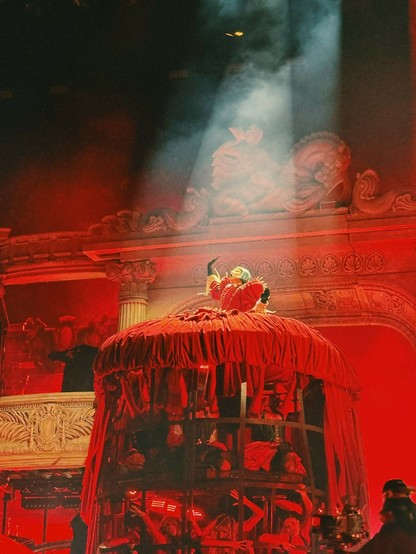 Lady Gaga in blood red Victorian-era dress. Her stage is lit up in red lights, evoking the feeling of hell. Underneath her dress' gigantic skirt is a cage holding people captive while they squirm and dance in pain.