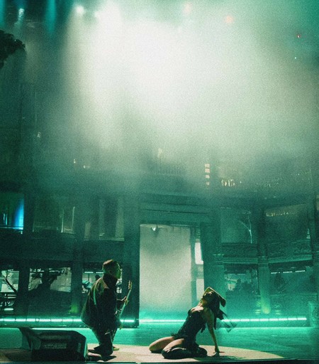 Lady Gaga dancing on the floor under the spotlight while a guitarist plays for her.