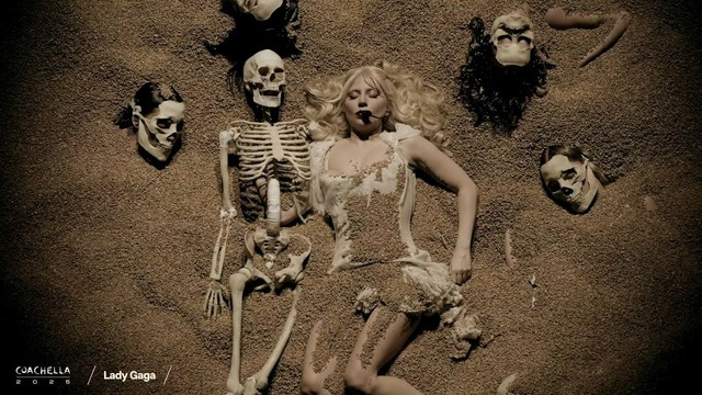 Lady Gaga laying buried underneath the sands surrounded by skeletons.