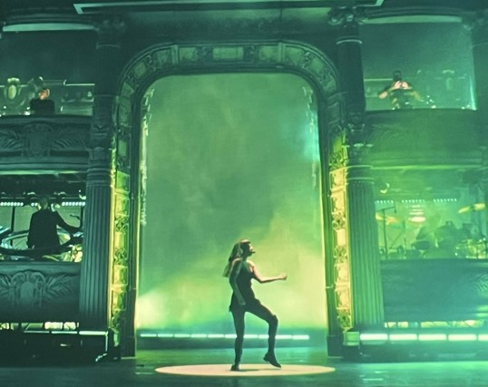 Lady Gaga dancing in front of a huge greco-roman entryway lit with green lights.