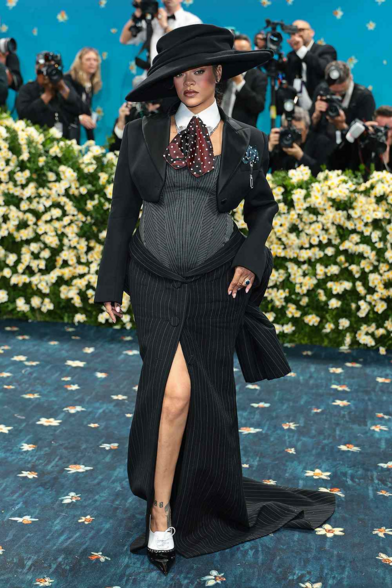 Rihanna wearing an oversized black hat, a cropped black suit on top of a denim body suit with a long pencil-cut skirt with a slit.