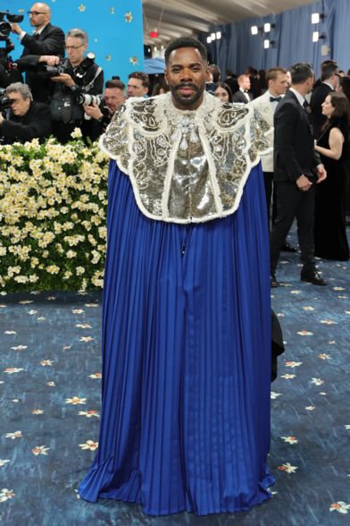 Colman Domingo wearing a deep blue pleated cloak underneath an oversized silver colar studded with diamonds.