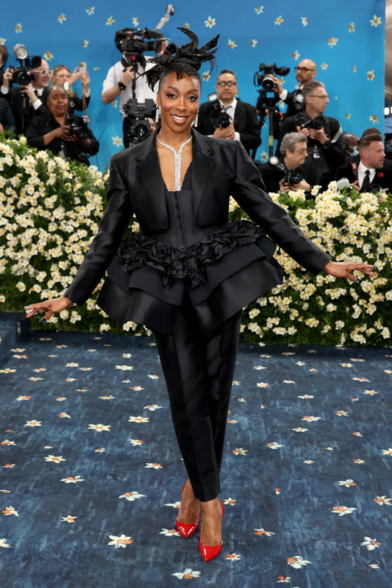 Ego Nwodim wearing a black cropped suit on top of a corset-like bodice that extends into a puffed up short skirt. She wears a pair of trousers underneath with a pair of glossy red stilletos.