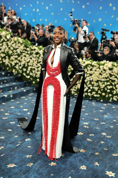 Ayo Edebiri is bringing bold elegance with a structured white gown adorned in dramatic red beadwork that loops down the torso and flows to the floor, creating a striking contrast. Paired with a sleek black coat featuring exaggerated shoulders and satin lapels, the whole look is powerful, modern, and unapologetically fashion-forward.