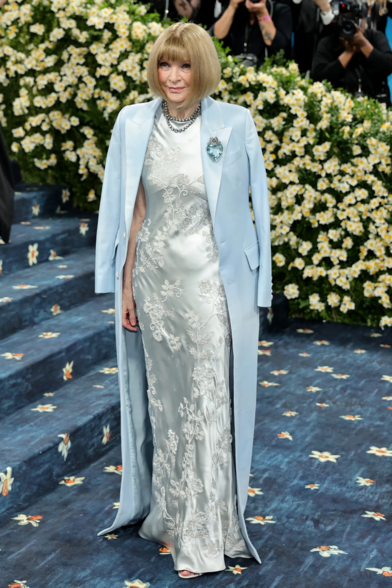 Anna Wintour. I don't even want to add alt text for this image, it's too boring. But she's wearing a satin long dress underneath a baby blue satin coat.
