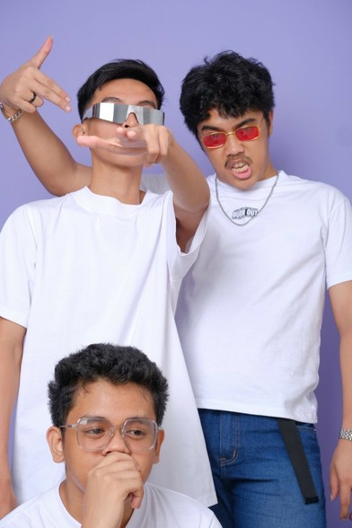 Three dudes in white shirt. One's wearing a pair of red sunglasses, gesturing a gun with his hands pointing it to another dude. The other dude is wearing silver sunglasses, also gesturing a gun with his hands but pointing it to the camera. The third dude is wearing a pair of regular square glasses, clutching his chin and mouth while looking off to the side in deep thought.