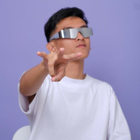 A guy in his early 20s wearing silver sunglasses gesturing a gang sign to the camera.