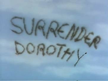 The Wicked Witch of the West writing "Surrender Dorothy" in the sky with the smoke from her broom.