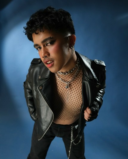 That same mysterious visionary echoing the same pose in a bolder transformation—draped in leather, mesh, and chains, with fierce makeup and piercings. The gaze remains intense, but now charged with unapologetic edge and raw attitude.
