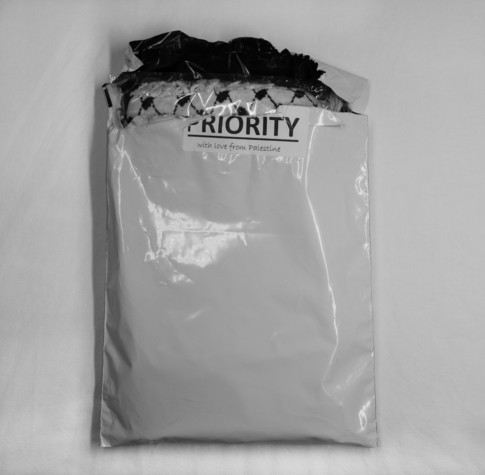 Bild: Schwarzweißfoto einer verpackten Kufiya, geöffnet, Aufkleber "Prority With love from Palestine".