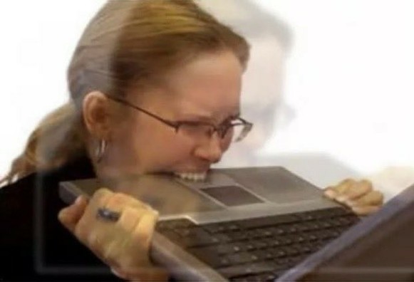 Middle-aged woman biting her laptop in frustration.