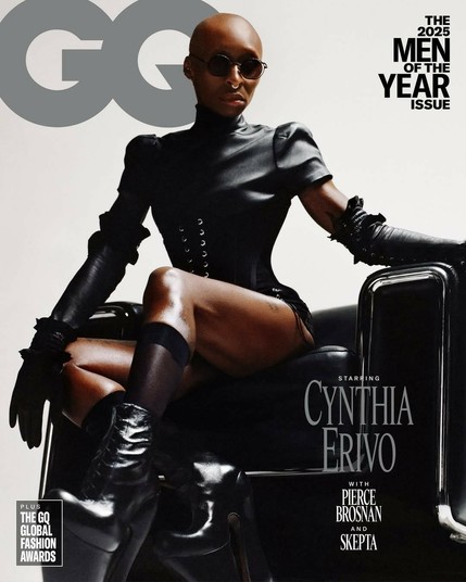 A high-contrast close-up of Cynthia Erivo on the GQ "Men of the Year Issue" cover, featuring her in a severe black leather outfit, including a corset and long gloves, while seated. She is bald, wearing dark, round sunglasses, and the text highlights her as the star, alongside Pierce Brosnan and Skepta.