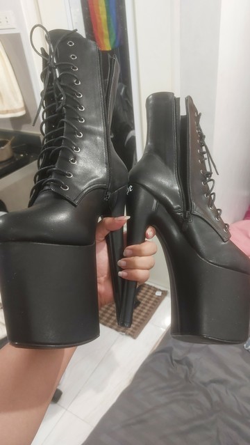 A pair of pleaser boots with 8-inch heels. I am holding both heels with one hand, showing my uncut nails to make it look more cunty.